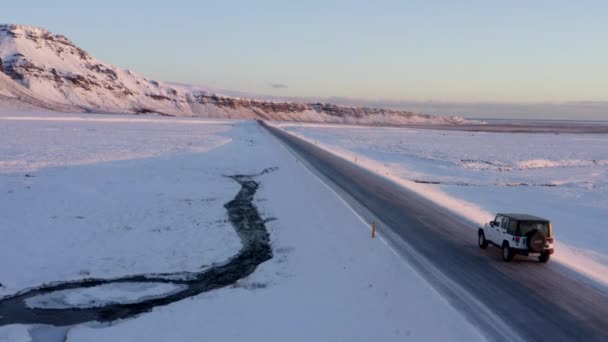 AERIAL: Volando además de Jeep en carretera nevada en Islandia al atardecer Invierno, Sol, Ártico — Vídeos de Stock