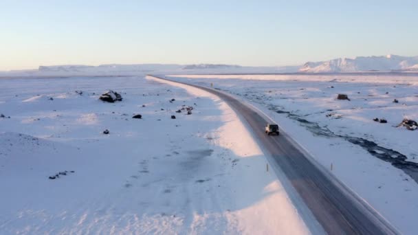 AERIAL: Paisagem Branca de Neve com Estrada seguindo Jeep na Islândia ao pôr do sol Inverno, Sol, Árctico — Vídeo de Stock