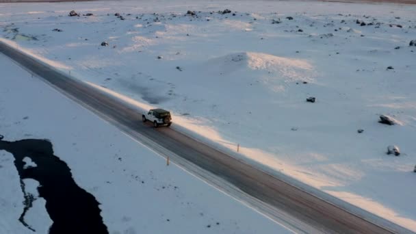 АЭРИАЛ: Летит джип по заснеженной дороге в Исландии на закате зимы, солнце, Арктика — стоковое видео