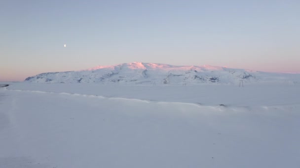 AERIAL:雪の白い山とピンクの太陽の光がアイスランドの冬、氷の上を打つ — ストック動画