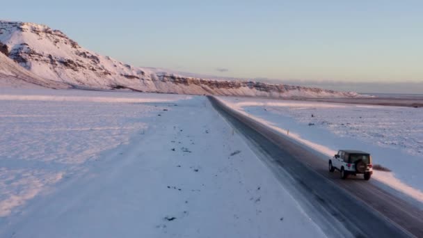 AERIAL: Flyger förutom Jeep på snöig väg på Island vid solnedgången med Sun Flair Winter, Sun, Arctic — Stockvideo