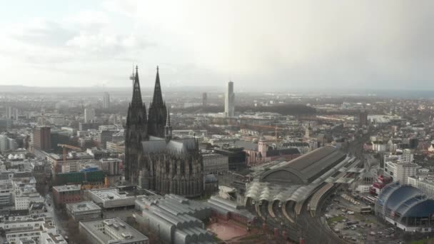 AERIAL: Rodeando la hermosa catedral de Colonia con la estación central de tren en la hermosa luz del sol brumosa — Vídeo de stock