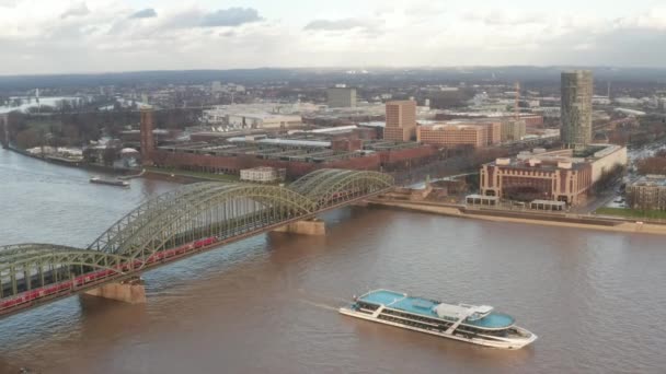 AERIAL: Sobre el casco antiguo de Colonia y vista del Rin y el puente de Hohenzollern con cruce de trenes y barco pasando el día soleado — Vídeo de stock