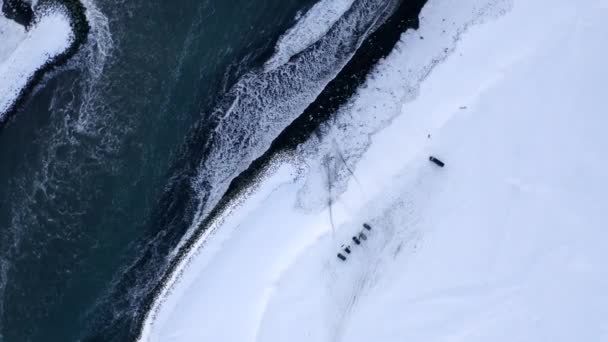 AERIAL:冬の雪、氷、波、水でアイスランドの白い北極雪の黒いビーチの鳥の景色 — ストック動画