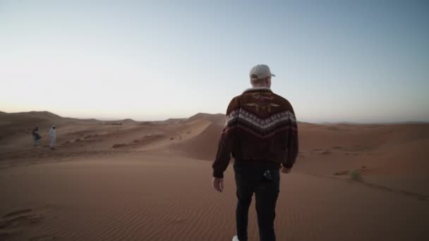 LÄGG MOTION: ADVENTUROUS YOUNG MAN WALKING TROUGH DESERT OVER DUNE OCH PICKING UP SAND — Stockvideo