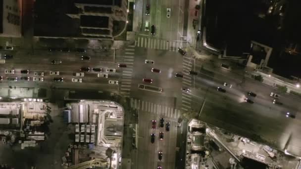 AERIAL: Overhead Rising on Intersection Street with big Construction Site and Holes in Ground at Night with Glowing Streets and City Car Traffic Lights — Stock Video