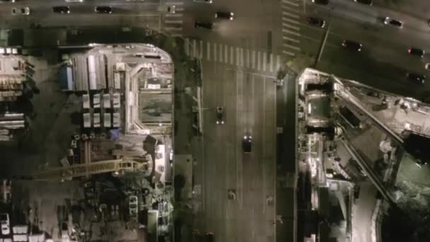 AERIAL: Widok na skrzyżowanie z dużym placem budowy i dziurami w ziemi w nocy z świecącymi uliczkami i miejskimi światłami drogowymi — Wideo stockowe
