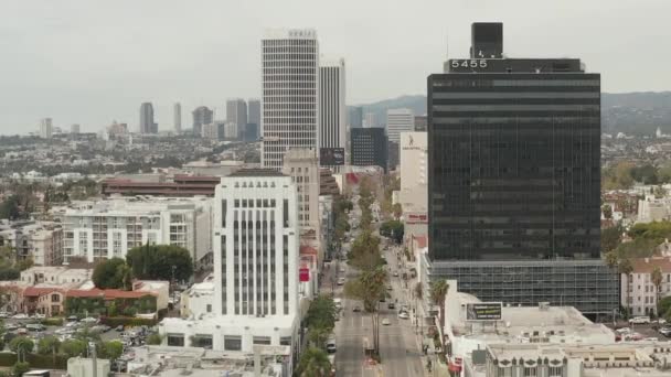 AERIAL: Vuelo sobre Wilshire Boulevard cerca de la calle y edificios con tráfico de coches en Los Ángeles, California en el día nublado — Vídeos de Stock