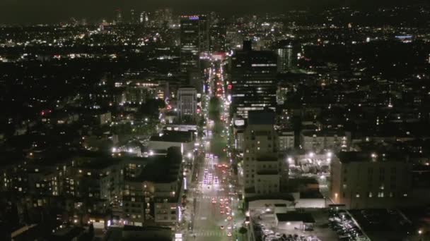 AERIAL: Vuelo sobre Wilshire Boulevard Street en Hollywood Los Ángeles por la noche con vista a las calles y los semáforos de coches urbanos — Vídeo de stock