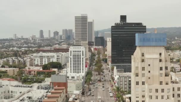 AERIAL: Flug über den Wilshire Boulevard in der Nähe von Straßen und Gebäuden mit Autoverkehr in Los Angeles, Kalifornien am bewölkten Tag — Stockvideo