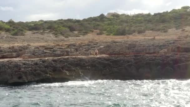 AERIAL: View On Waves Crashing into Rocks, Cliff Coast on Sunny Day with guy sitting on rocks on Mallorca Island Sunny Weather, Sunshine — Stock Video