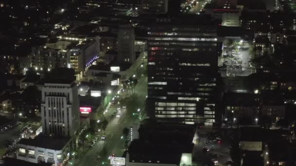 AERIAL: Sobre Wilshire Boulevard en Hollywood Los Ángeles por la noche con calles brillantes y semáforos de coches urbanos — Vídeo de stock