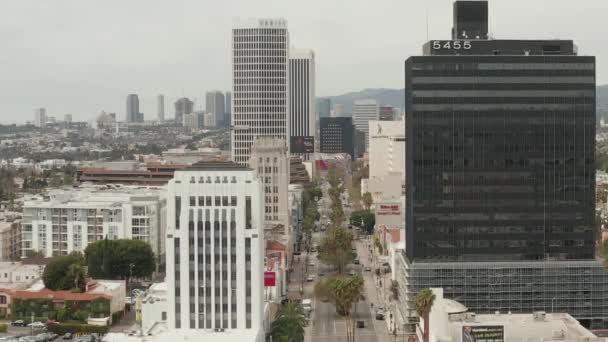 AERIAL: Vuelo sobre Wilshire Boulevard cerca de la calle y edificios con tráfico de coches en Los Ángeles, California en el día nublado — Vídeos de Stock