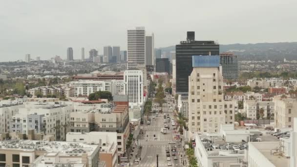 AERIAL: Flug über den Wilshire Boulevard in der Nähe von Straßen und Gebäuden mit Autoverkehr in Los Angeles, Kalifornien am bewölkten Tag — Stockvideo