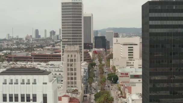 AERIAL: Flug über den Wilshire Boulevard in der Nähe von Straßen und Gebäuden mit Autoverkehr in Los Angeles, Kalifornien am bewölkten Tag — Stockvideo