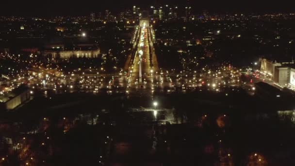 AERIAL: Vuelo en avión no tripulado inverso desde la Torre Eiffel, Tour Eiffel en París, Francia por la noche con luces de ciudad — Vídeo de stock