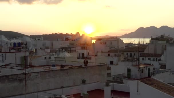 AERIAL: Man op het dak van Small Town huis met haven op Tropisch eiland met boten en oceaan bij zonsopgang met bergen in achtergrond vakantie, reizen, zonsondergang — Stockvideo