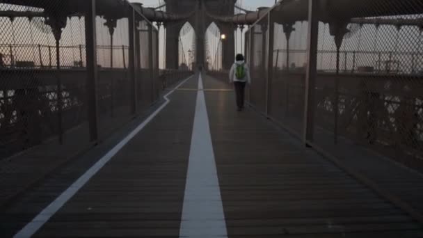 Brooklyn Bridge mit einer Frau, die frühmorgens bei Sonnenaufgang im schönen Sonnenlicht im Sommer spaziert — Stockvideo