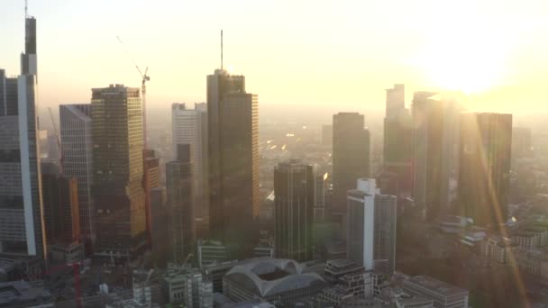 AERIAL: Vista de Fráncfort del Meno, Alemania Skyline con sunflair entre rascacielos en Beautiful Sunset Sunlight en Winter Haze — Vídeos de Stock