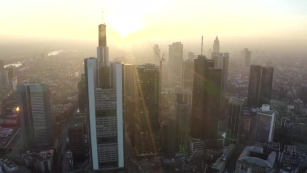 AERIAL: Vista de Fráncfort del Meno, Alemania Skyline con sunflair entre rascacielos en Beautiful Sunset Sunlight en Winter Haze — Vídeos de Stock