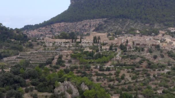 AERIAL: Valldemossa in de bergen met uitzicht op kasteel in de verte en straat met auto 's op Tropisch eiland Mallorca, Spanje op zonnige dag Vakantie, Reizen, Zonnig — Stockvideo