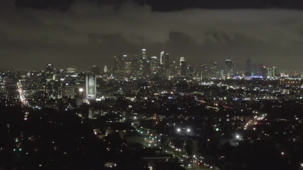 АЭРИАЛ: Над темным Голливудом Лос-Анджелеса ночью с облаками над центром города и городскими огнями — стоковое видео