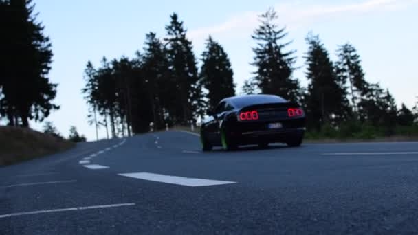 Lassú mozgás: fekete Ford Mustang autó hajtott ki a hegyen, erdei út napsütéses út, izom autó — Stock videók