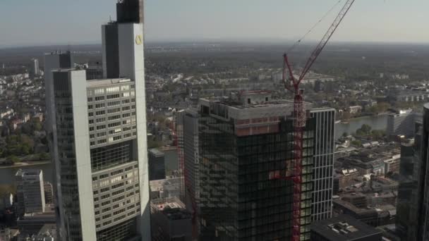 AERIAL: Close Up Zicht op wolkenkrabber bouwplaats in stedelijke omgeving met stadsverkeer en reflecties in toren op zonnige dag in Frankurt am Main Duitsland — Stockvideo