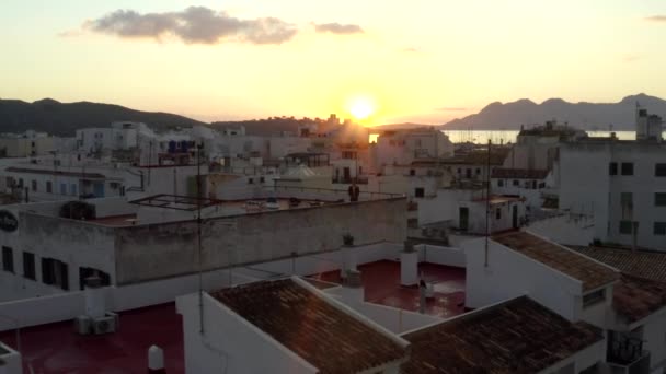 AERIAL: Guy de pé no telhado da casa Small Town com Porto na Ilha Tropical com Barcos e Oceano ao Nascer do Sol com Montanhas no Fundo Férias, Viagens, Pôr do sol — Vídeo de Stock