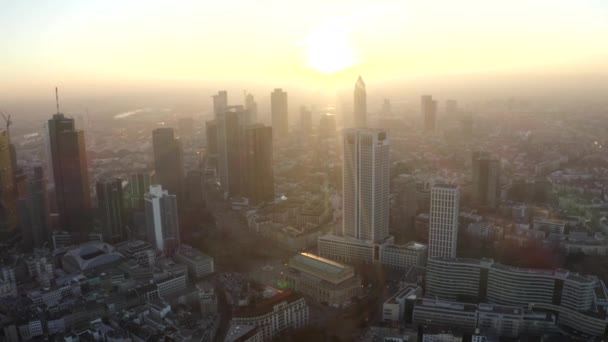 AERIAL: Vista de Fráncfort del Meno, Alemania Skyline con sunflair entre rascacielos en Beautiful Sunset Sunlight en Winter Haze — Vídeos de Stock