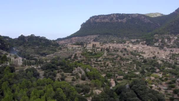 AERIAL: Valldemossa in de bergen met uitzicht op kasteel in de verte en straat met auto 's op Tropisch eiland Mallorca, Spanje op zonnige dag Vakantie, Reizen, Zonnig — Stockvideo