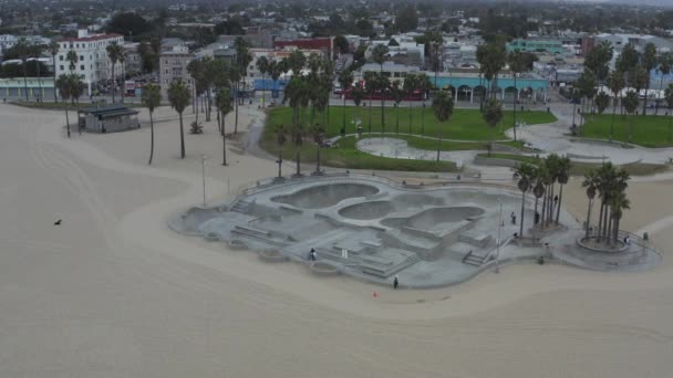 АЕРІАЛ: поверніть навколо Венеціанського пляжного скейтпарку з велосипедами і пальмами вранці, Cloudy Los Angeles, California — стокове відео