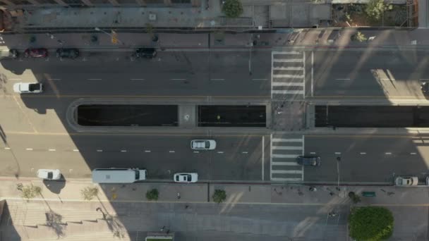 助手：年轻人躺在街上慢慢地鸟瞰飞机在美丽的日出光中飞越洛杉矶市中心，俯瞰着摩天大楼的屋顶和经过的车辆 — 图库视频影像