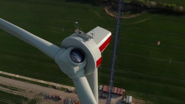 AERIAL: Крупный план строящейся ветряной турбины, строящейся на богатом зеленом сельскохозяйственном поле — стоковое видео