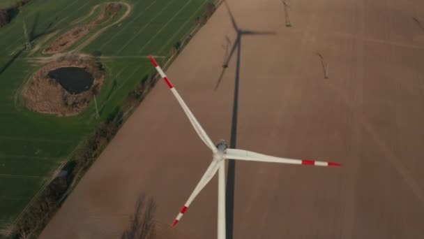 AERIAL: Zbliżenie ujęcia turbiny wiatrowej, Młyn obracający się siłą wiatru generującego energię odnawialną w ekologiczny sposób dla planety nad pięknym polem zielonego rolnictwa — Wideo stockowe