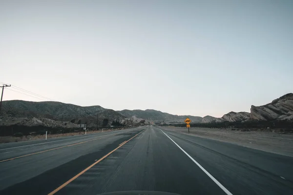 Estrada vazia na Califórnia Logo após o pôr-do-sol com sinal de estrada amarelo e montanhas na distância durante a pandemia do Coronavirus — Fotografia de Stock