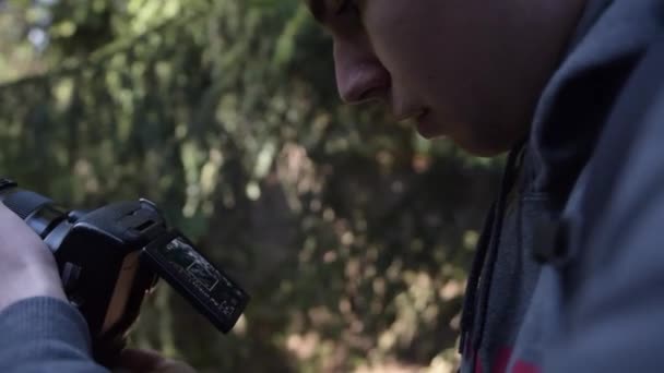Joven, Fotógrafo Tomando fotos con cámara en el bosque en verano con hermosa luz del sol — Vídeos de Stock