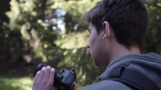 MOCIÓN LENTA: Joven, Fotógrafo tomando fotos con cámara en el bosque en verano con hermosa luz del sol — Vídeos de Stock