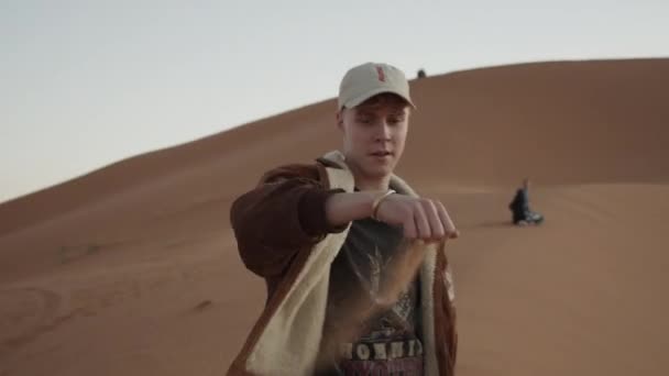 ADVENTUROUS YOUNG MAN PICKING UP SAND FROM THE SAHARA DESERT IN BEAUTIFUL SUNSET LIGHT — Stock Video