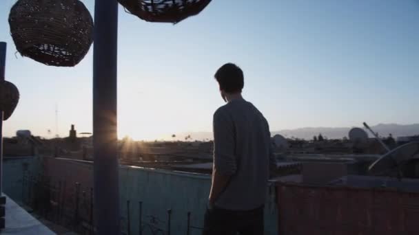 スローモーション:美しい青とオレンジの色で早朝の日の出と屋上テラスを歩く若い男 — ストック動画