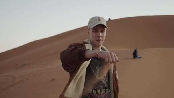 SLOW MOTION: ADVENTUROUS YOUNG MAN PICKING UP SAND FROM THE SAHARA DESERT IN BEAUTIFUL SUNSET LIGHT — Stock video