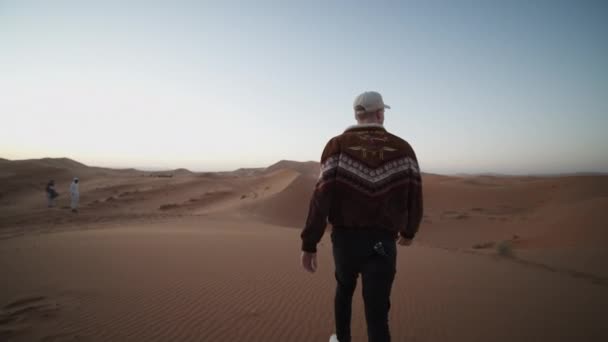 ADVENTUROUS JUNGE MANN WANDERUNG TROUGH DESERT ÜBER DUNE UND PICKING UP SAND — Stockvideo