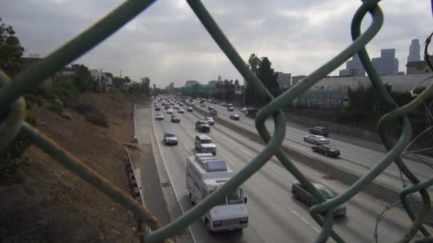 チェーンリンクフェンスを介してロサンゼルスで忙しい高速道路交通の眺め曇りの日にスローモーションで — ストック動画