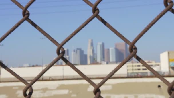 Zicht op Los Angeles Downtown Skyline via ketting link hek op blauwe Sky Summer Day in SLOW MOTION — Stockvideo