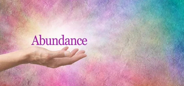 Attract Abundance - female open palm hand with a deep pink ABUNDANCE floating above on a pink and blue rustic stone background with copy space