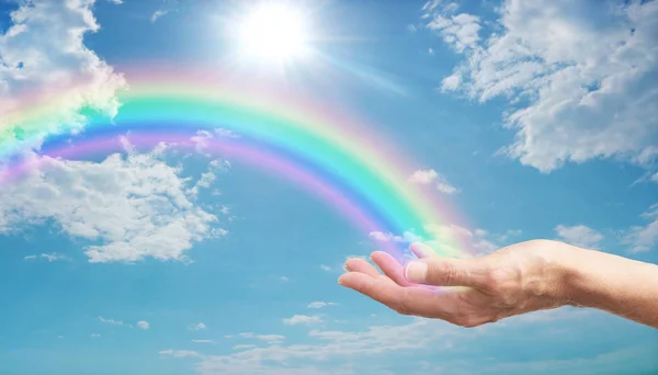 ここでは ふわふわの雲と明るいチェリーサン バーストと青い空の間でアーク放電明るい虹と女性の手 あなたのための美しい虹 — ストック写真