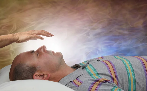 Healer Channelling White Healing Energy - female with hand held a few inches above a male patient's face against a flowing ethereal energy formation background