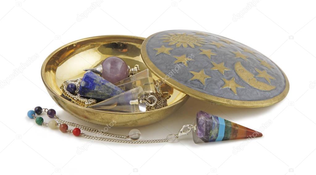 Selection of Radionics Dowsing Pendants - Brass dish on a white background containing three different dowsing pendulums and one Chakra coloured pendant laid in front
