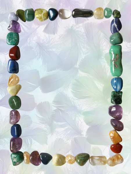 Rectangular Portrait Healing Crystal Border Frame - A border of carefully arranged multi colored tumbled  crystals isolated on blue green grey coloured negative bird feathers