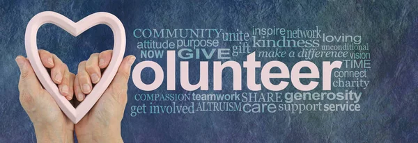 志愿工作是爱情世界的一种表现 女性的手牵着苍白的粉红的心脏框架 在蓝色的 质朴的石头效果背景上 除了一个相关的云彩字外 还能组成Volunteer — 图库照片